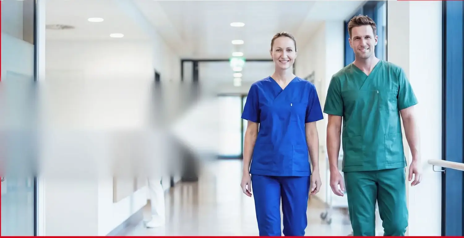Zwei Mitarbeitende in medizinischer Berufsbekleidung in einem Klinikflur